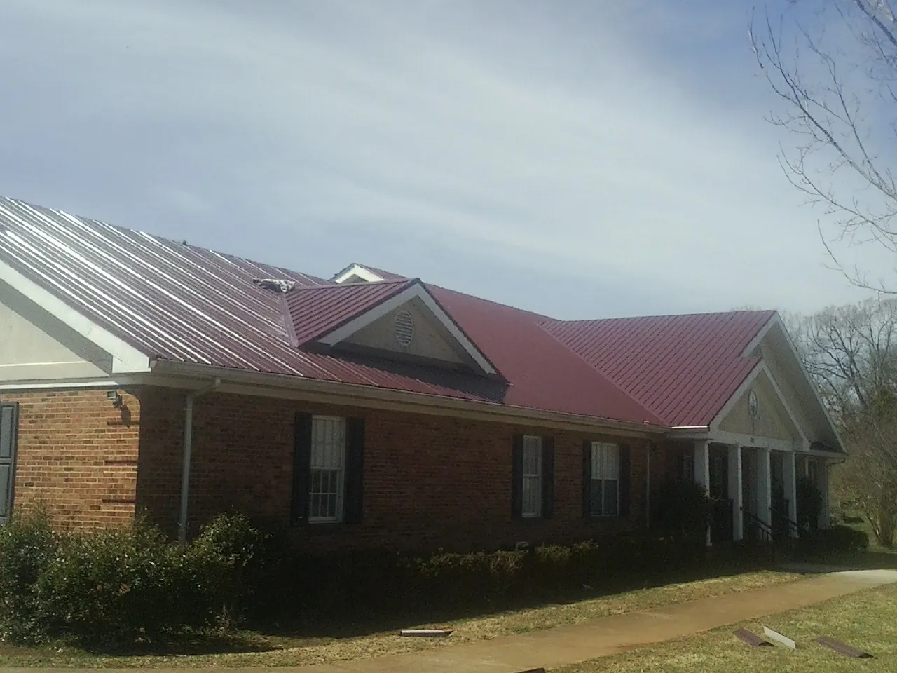 Red metal roof with gabled entries on a long brick building, from a Hail Damage Roof Repair job in University Park