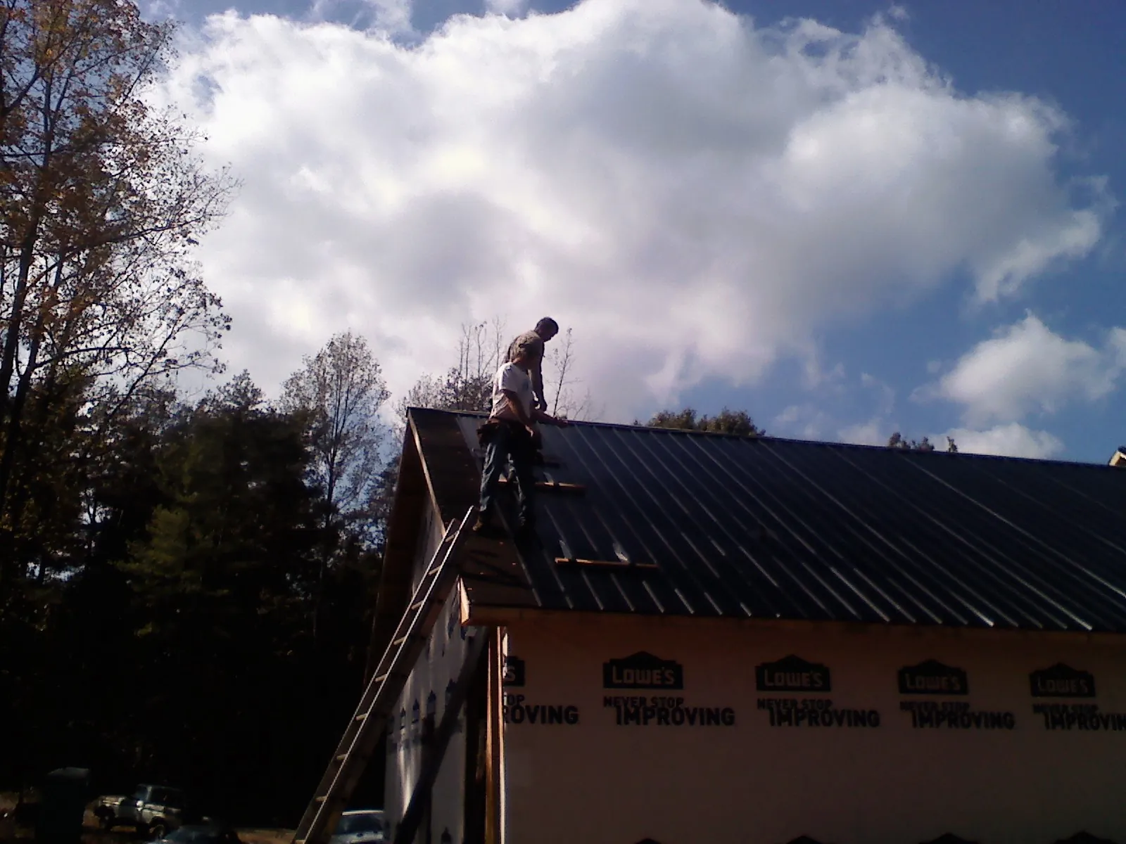 Roofer fastening dark metal panels high against a cloudy sky, from a Roof Inspection job in University Park